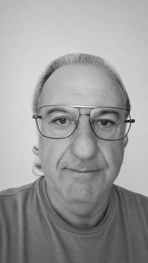 Black and white headshot portrait of an older man wearing glasses and a casual shirt against a plain background